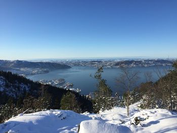 Scenic view of snowcapped fløyen top against clear blue sky and the  fjord  in bergen,, norway