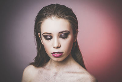 Close-up of shirtless young woman against colored background