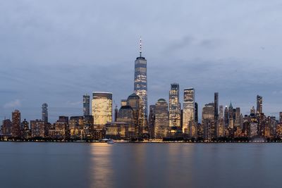 Illuminated buildings in city against cloudy sky