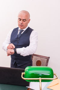 Businessman looking at wristwatch while standing laptop on desk at office