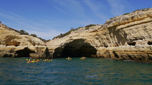 Scenic view of rock formation in sea against sky with group of canoes 