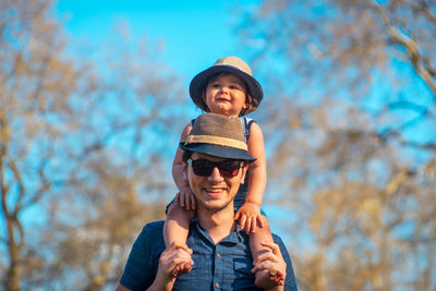 Portrait of happy father carrying son on shoulders against trees