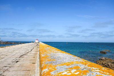 Footpath leading towards sea against blue sky