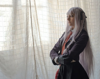 Side view of young woman standing against curtain