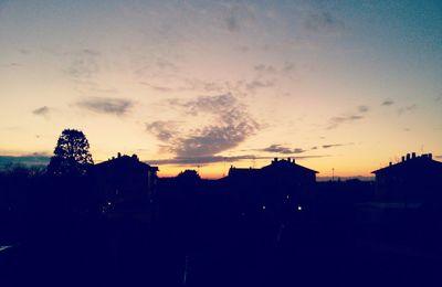 Silhouette of buildings against cloudy sky at sunset