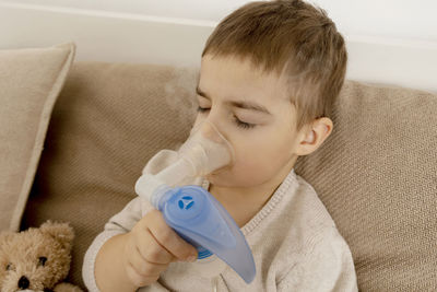 Sick little boy with inhaler for cough treatment. unwell kid doing inhalation on his bed. 