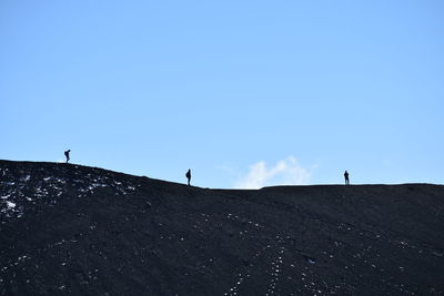 Low angle view of hikers standing on mountain against clear blue sky
