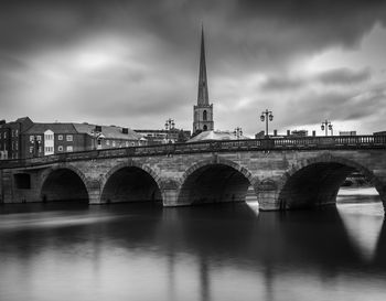 Arch bridge over river by buildings against sky