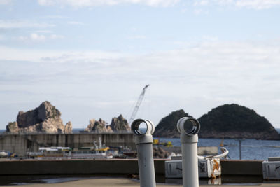 Metallic structure by sea against buildings at the seaside against sky