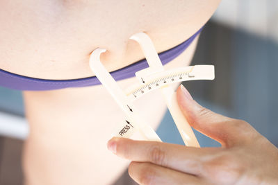 Midsection of woman checking waist fat with caliper