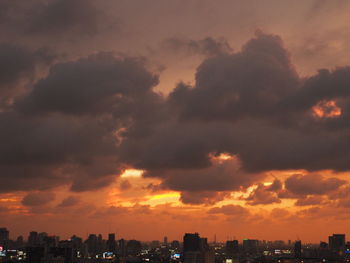 Silhouette cityscape against dramatic sky during sunset