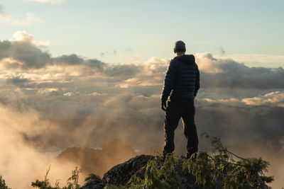 Rear view of man standing on cliff against cloudy sky