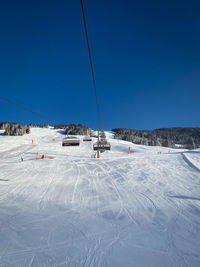 Ski lift over snow covered field against clear blue sky