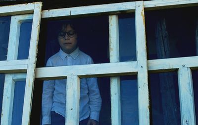 Low angle view of boy wearing eyeglasses standing at window