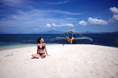 Young woman sitting by sea against sky