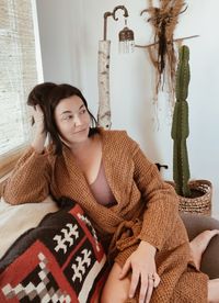 Smiling woman looking away while sitting on sofa at home