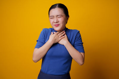 Smiling young woman standing against yellow background