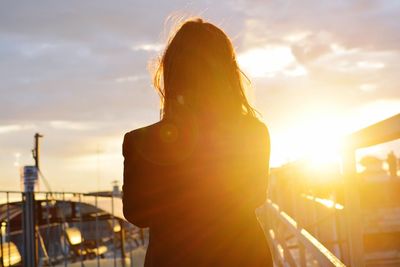 Rear view of woman standing against sky during sunset