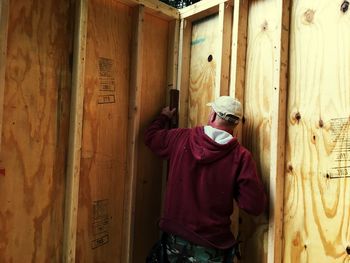 Rear view of man measuring wooden wall