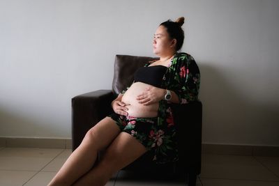 Thoughtful pregnant woman looking away while sitting on armchair at home