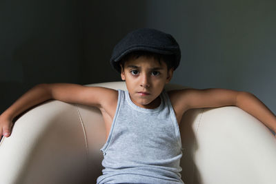 Portrait of boy wearing hat sitting against wall