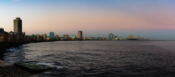 Sea by buildings against sky during sunset in city