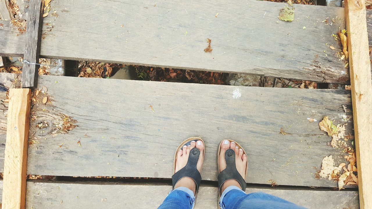 low section, person, shoe, personal perspective, standing, human foot, footwear, high angle view, men, lifestyles, jeans, directly above, part of, unrecognizable person, day, outdoors, wood - material