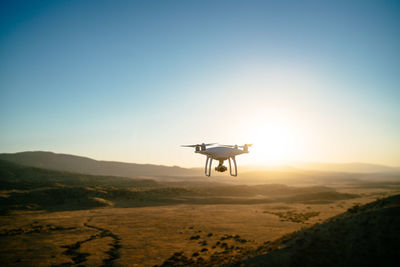 Quadcopter flying over landscape against clear sky during sunset
