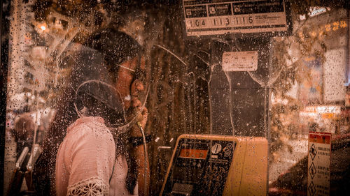 Teenage girl talking in wet telephone booth during rain