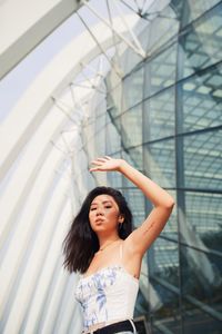 Young woman shielding eyes standing against building in city