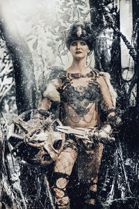 Portrait of woman in costume with weapon standing in forest