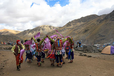 People in traditional clothing dancing on sand against mountains and sky