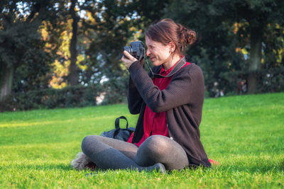 Full length of woman photographing while sitting on land