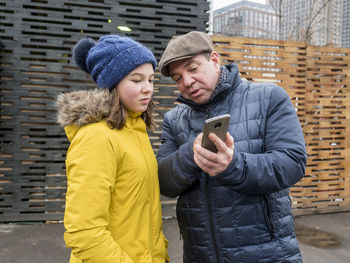 Father showing mobile phone to daughter while standing on street during winter