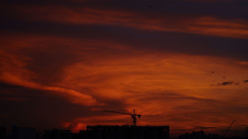 Silhouette of factory against orange sky