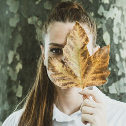 Portrait of young woman holding leaf during autumn