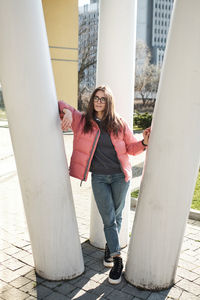 Happy young girl in glasses wearing a pink jacket and jeans