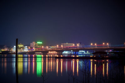 Illuminated buildings by river against sky at night