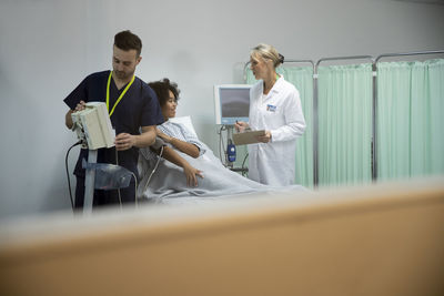 Nurse operating blood pressure machine with patient and doctor talking in background