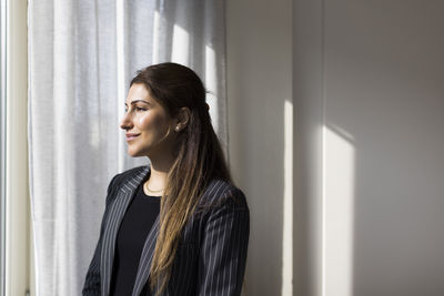 Smiling female real estate agent looking through window at new home