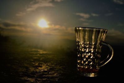 Close-up of glass of water against sky during sunset