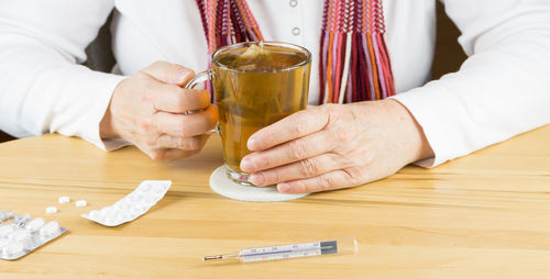 Midsection of woman having tea and medicine at table