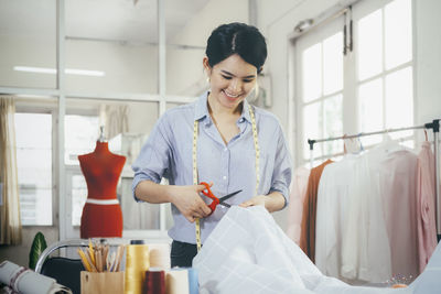 Smiling fashion designer cutting textile at boutique