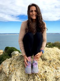 Portrait of smiling woman on rock by sea against sky