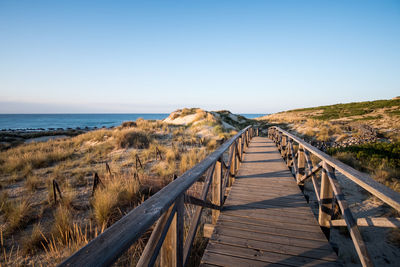 Boardwalk leading towards sea against clear sky