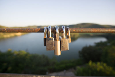 Close-up of padlocks hanging on river against sky