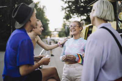 Happy non-binary person talking with woman by friends