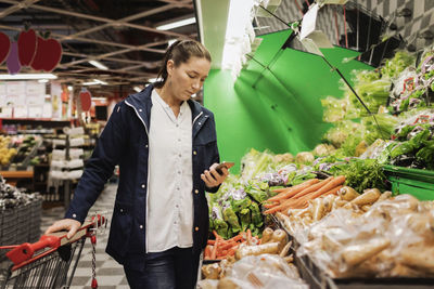 Woman using smart phone while buying groceries in supermarket