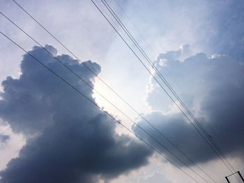 Low angle view of birds perching on cable against cloudy sky