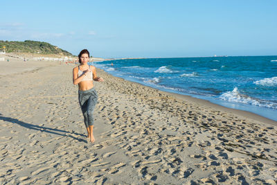 Portrait of young woman jogging at beach against sky